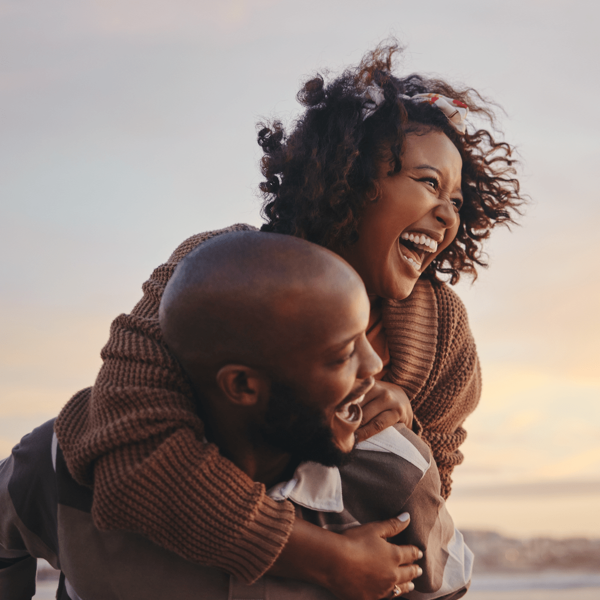 A couple laughing on the beach at sunset, enjoying a moment of joy together.